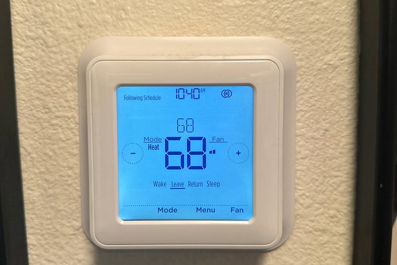 Photo: Thermostat Settings: On vs. Auto Photo of a digital thermostat mounted on a wall with a blue light.