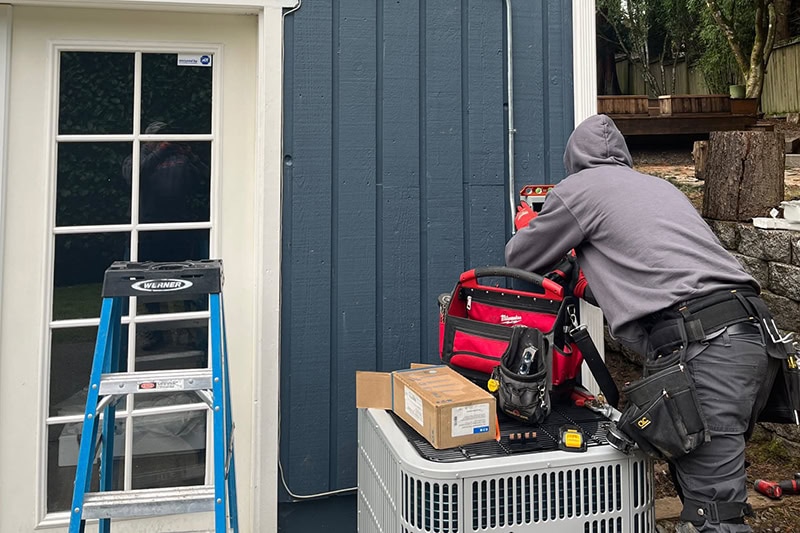 Photo of an HVAC Technician performing maintenance on a unit installed outside of a home.