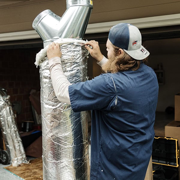 Lifetime Heating, Cooling, Plumbing & Electric technician holding an air duct outside a customers home.