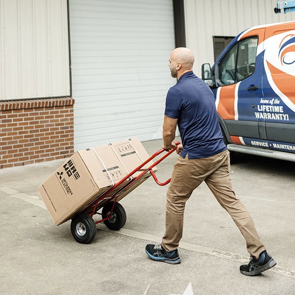 Lifetime Heating, Cooling, Plumbing & Electric employee walking towards warehouse with box.
