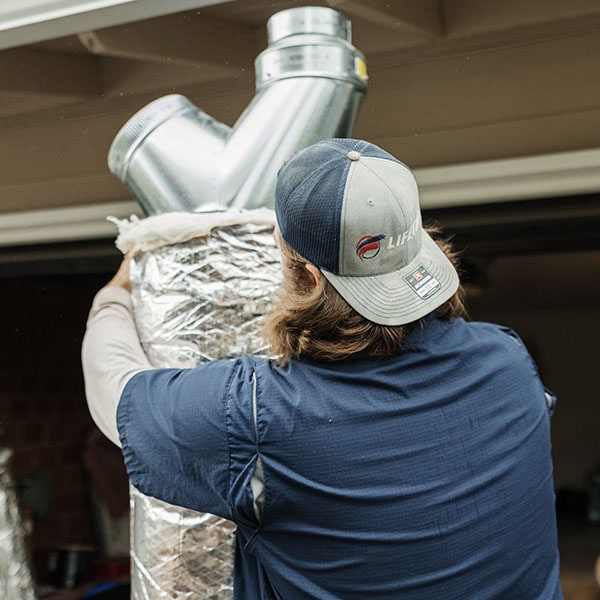 Lifetime Heating, Cooling, Plumbing & Electric holding an air duct outside a customers home.