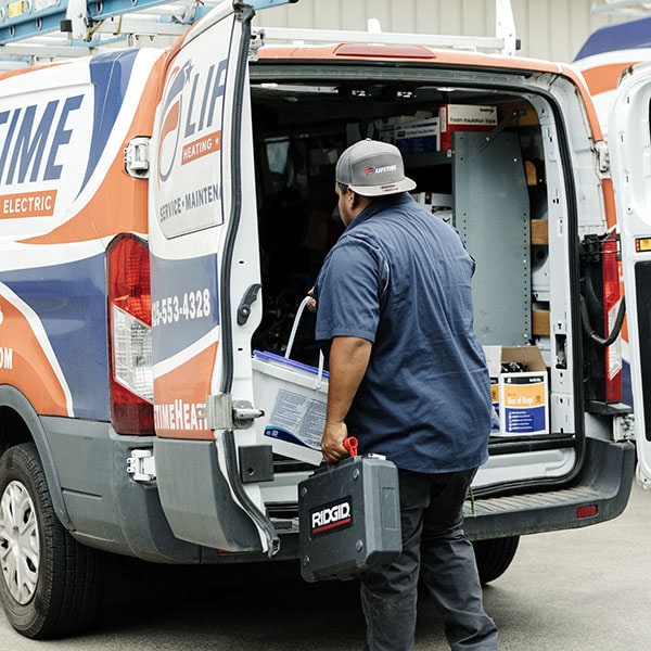 Lifetime Heating, Cooling, Plumbing & Electric technician putting small tub and tool box into the back of company van.