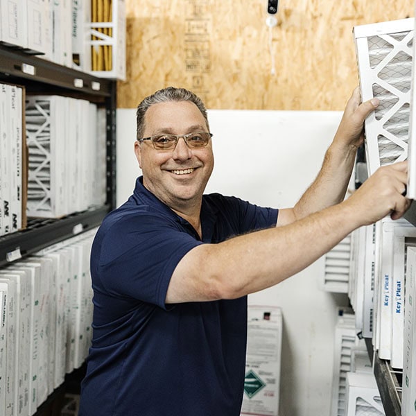 Lifetime Heating, Cooling, Plumbing & Electric employee holding air filter in warehouse.