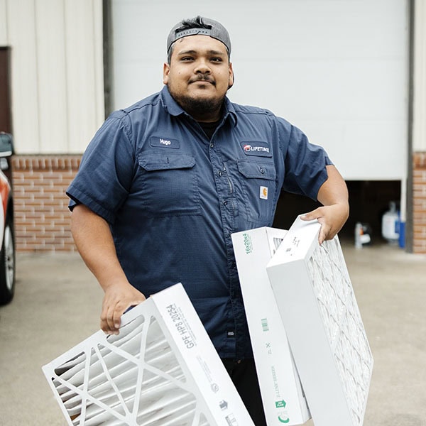 Lifetime Heating, Cooling, Plumbing & Electric technician holding air filter outside warehouse.